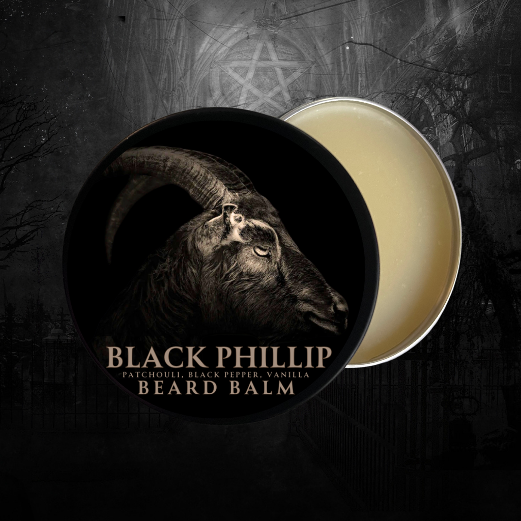 A small tin of Glamgoria Black Phillip Beard Balm with a silver lid and dark occult branding. Set on rustic wood with candlelight.