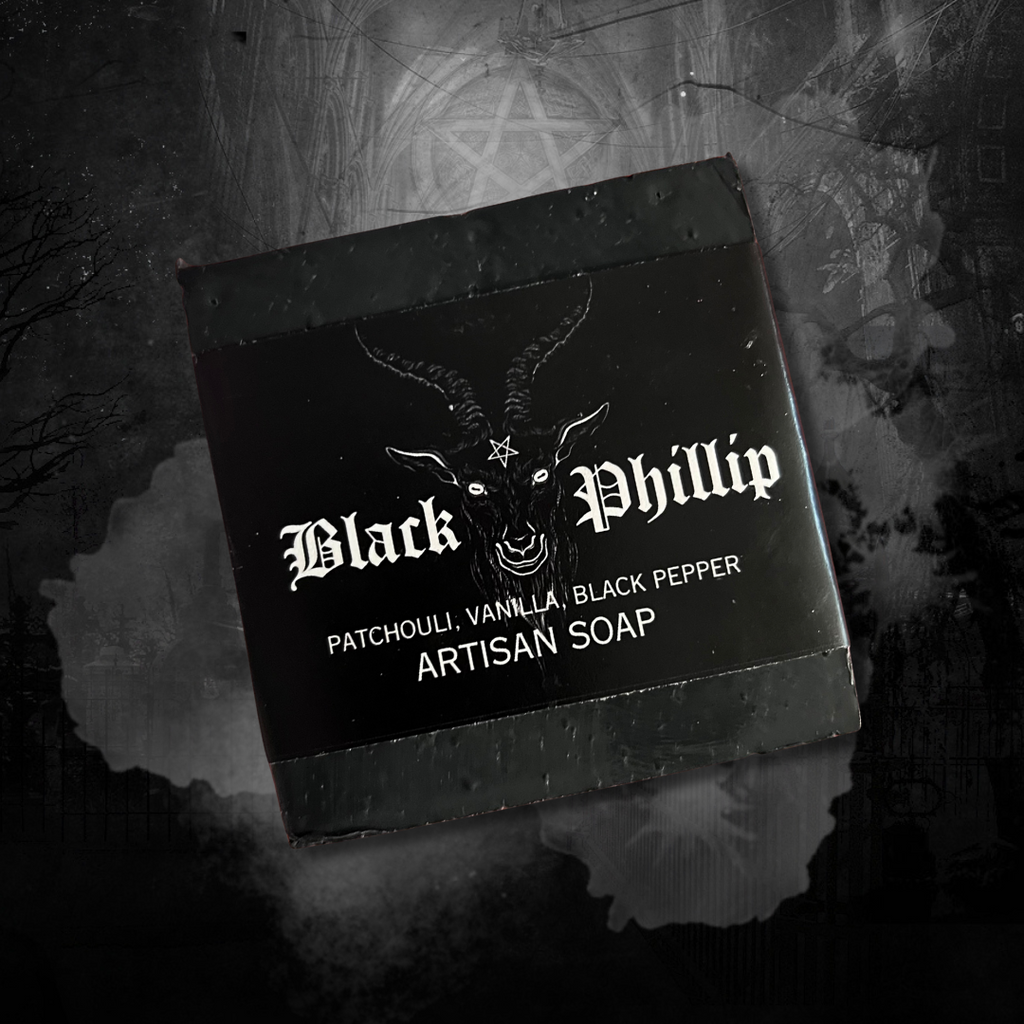 A handcrafted black soap bar shaped like a horned goat head. Subtle shimmer with red eye accents. Bath tub and ritualistic setting.