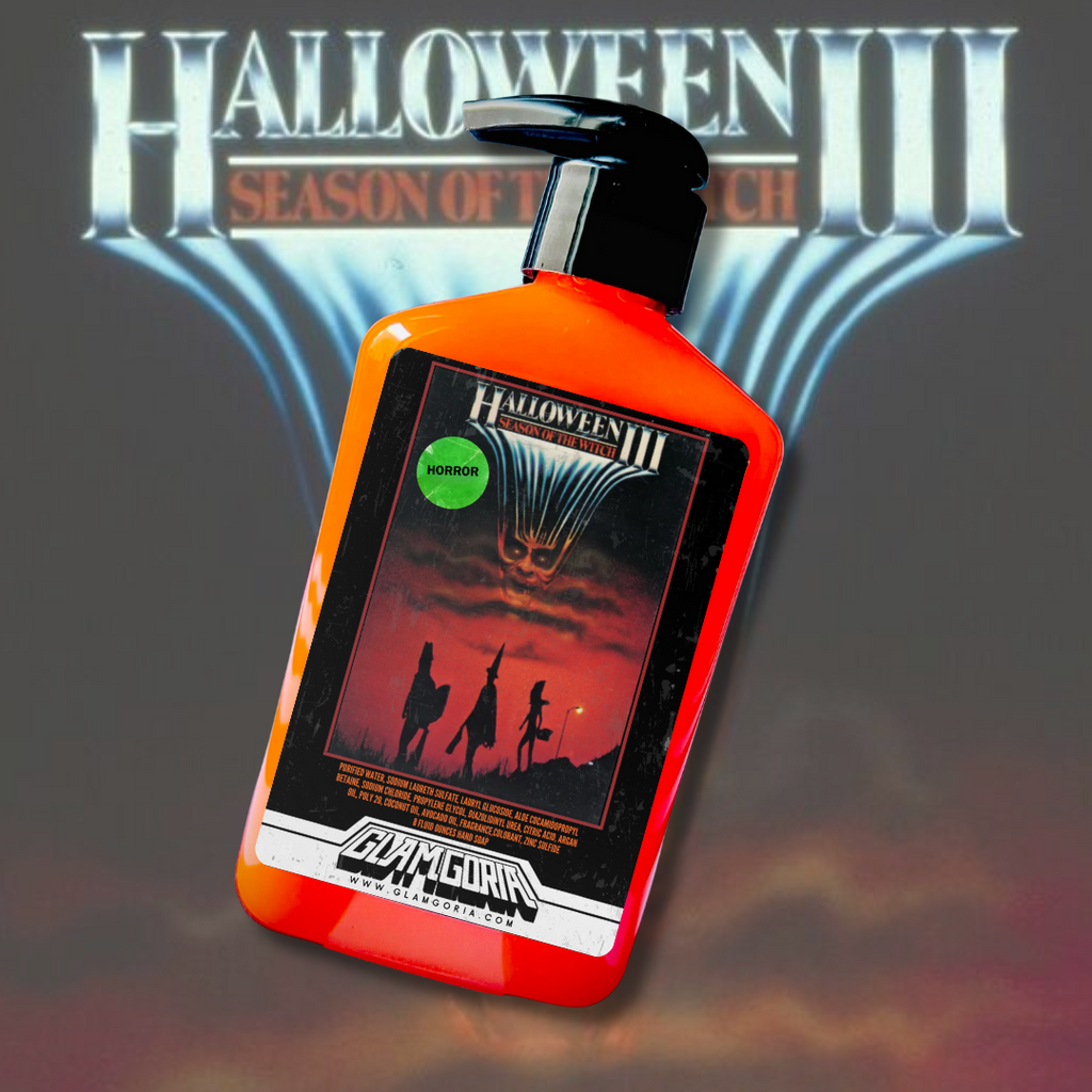 A bright orange bottle of Glamgoria’s Halloween III hand soap, with a vintage horror movie label featuring silhouettes of trick-or-treaters under a glowing, ominous mask design. Background shows the Halloween III title and logo.
