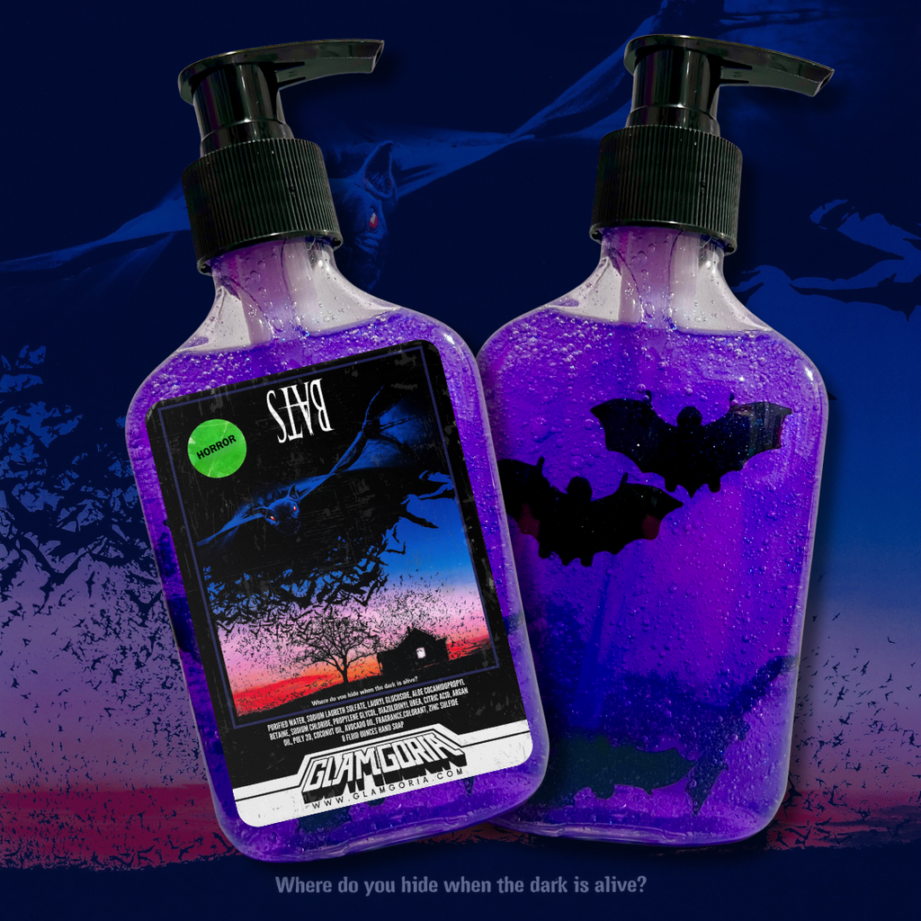 Two bottles of Glamgoria’s Bats hand soap with floating toy bats in purple gel. One bottle shows a horror movie-inspired label featuring bats flying over a cabin at dusk.