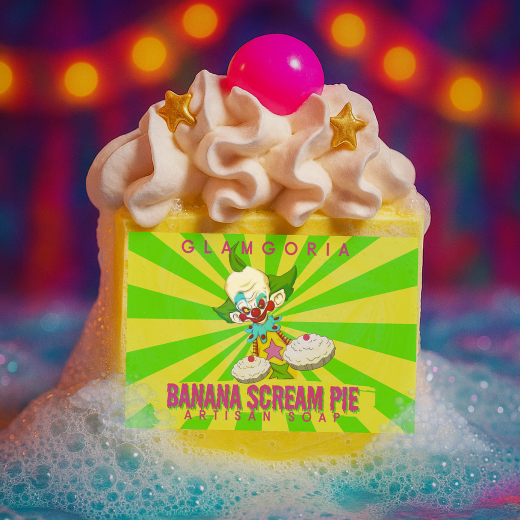 Bright yellow artisan soap inspired by Killer Klowns from Outer Space, topped with fluffy whipped soap frosting, a hot-pink sphere, and gold star embeds. The label shows a creepy clown illustration with “Banana Scream Pie.” Soap sits in colorful bubbles with a carnival-themed bokeh background.