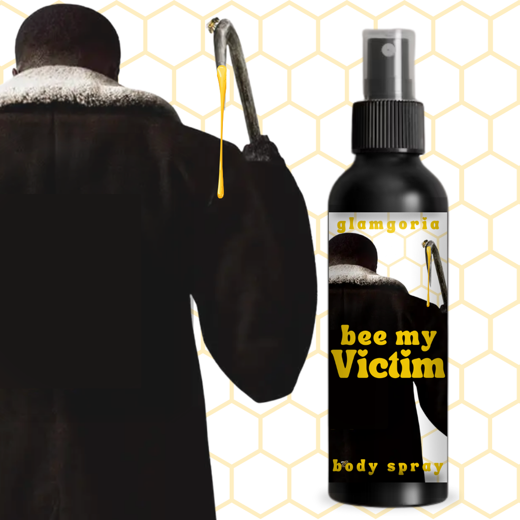 Clear body spray bottle filled with golden yellow liquid labeled “Bee My Victim” by Glamgoria, inspired by classic horror and honey imagery

