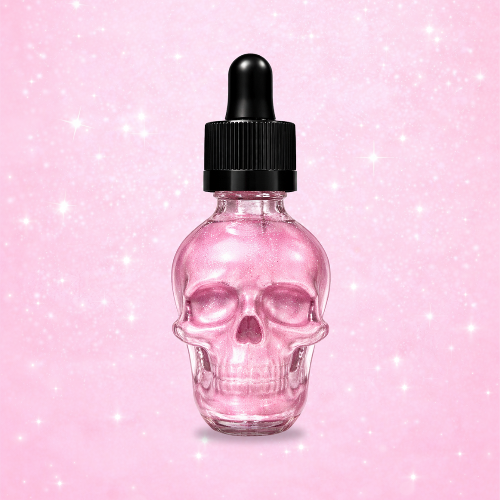 Pink sparkling bath and body oil in a clear skull-shaped glass dropper bottle with a black cap, set against a soft pink glitter background.