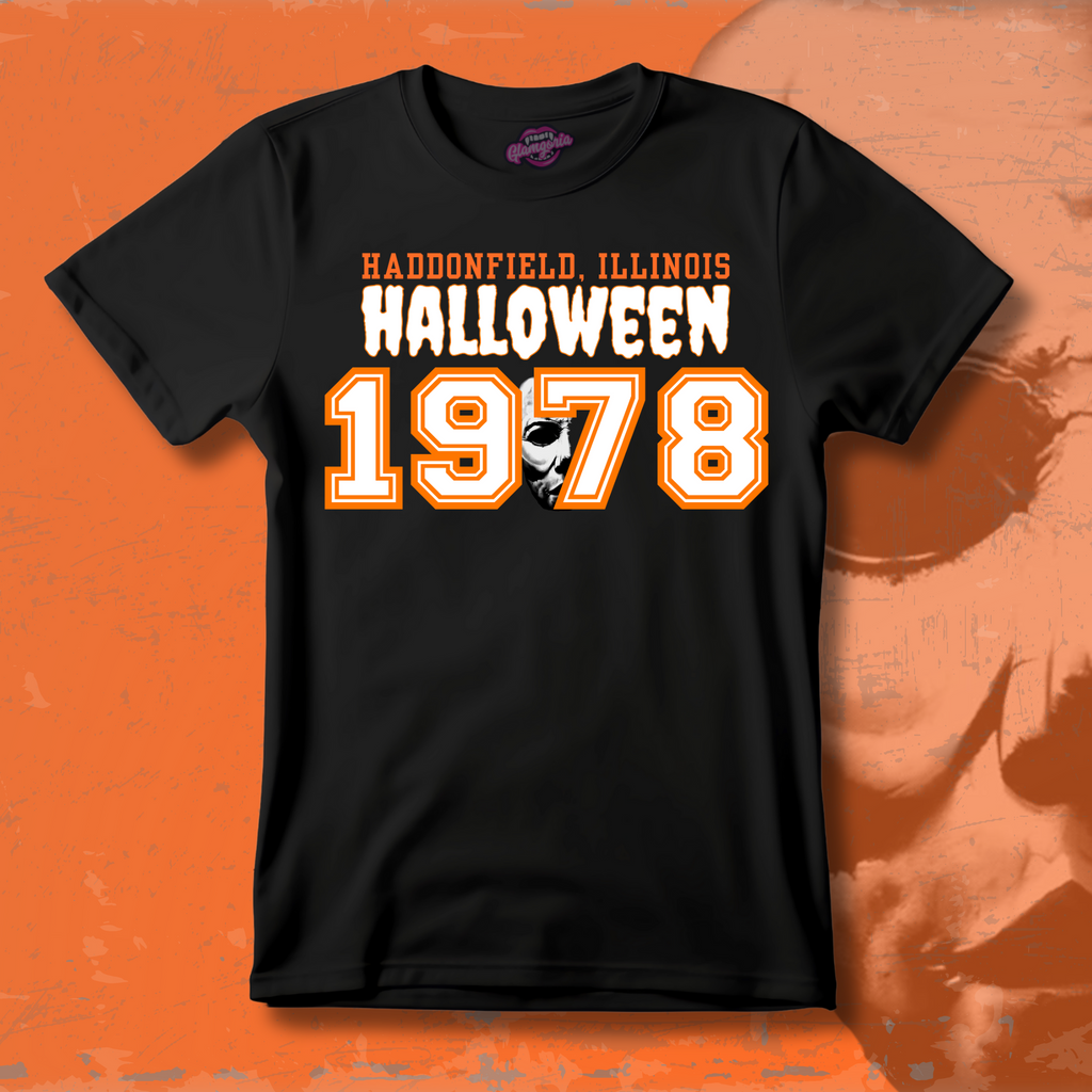 Black cotton T-shirt featuring Glamgoria’s original design with “Haddonfield, Illinois Halloween 1978” in bold varsity-style orange and white text, including Michael Myers’ mask inside the number zero.