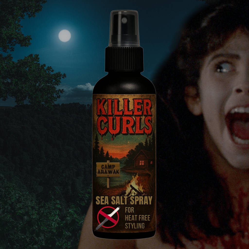 A spooky promotional image for Glamgoria’s “Killer Curls” Sea Salt Spray, inspired by the horror film Sleepaway Camp. The product is shown in a sleek black spray bottle with a retro, horror-camp-themed label. The label reads “Killer Curls” in blood-dripping red letters above a lakeside cabin scene, complete with pine trees, a fiery campfire, and a wooden sign reading “Camp Arawak.” Below, the text says “Sea Salt Spray for Heat Free Styling,” featuring a red circle with a slash through a curling iron icon. I