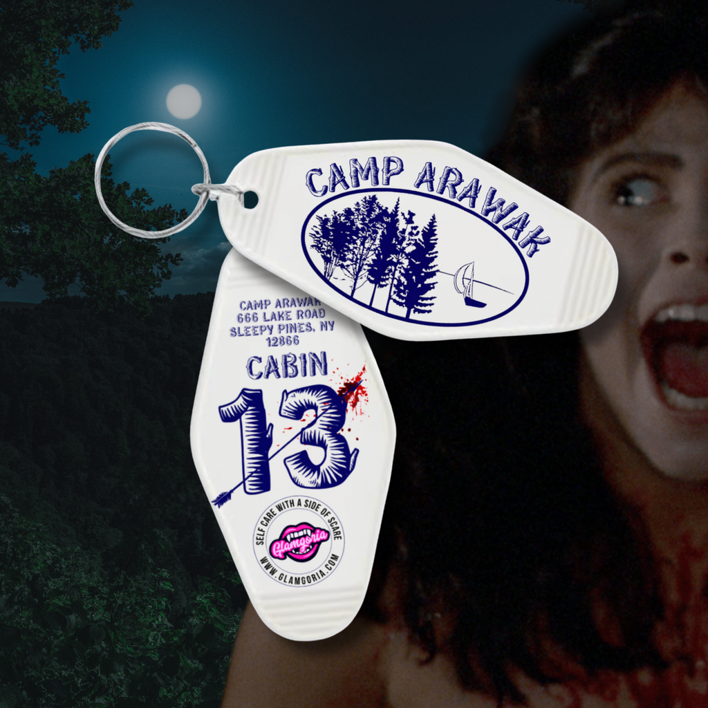 Vintage motel-style horror keychain for Camp Arawak with trees, oar, and Cabin 13 design from Sleepaway Camp. White key tag with blood splatter, creepy summer camp aesthetic.
