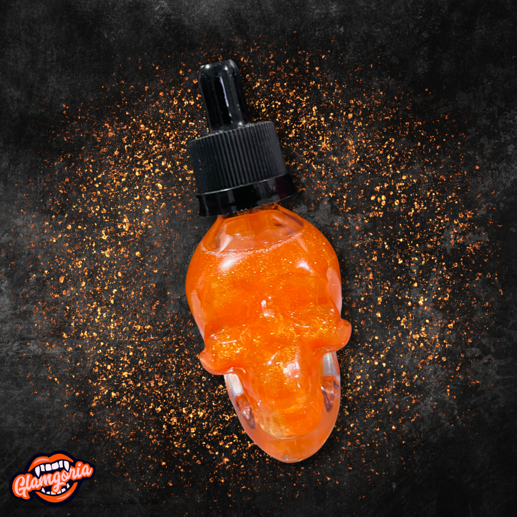 
A skull-shaped dropper bottle filled with shimmering orange bath and body oil. The bottle has a black dropper cap, and the oil inside has a glittery effect, giving it a magical, glowing appearance. The background is dark with scattered orange sparkles surrounding the bottle, enhancing the product’s witchy, autumnal vibe.