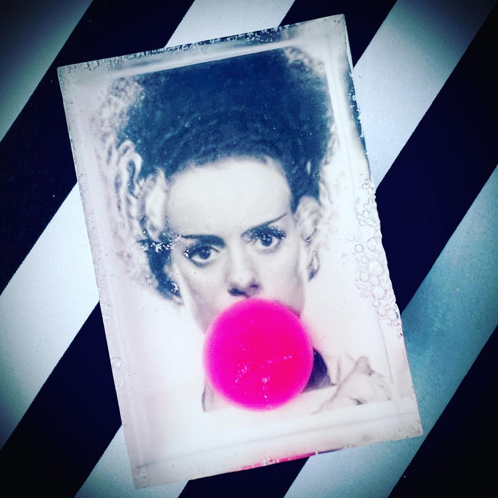 Clear rectangular soap with a black-and-white image of the Bride of Frankenstein blowing a bright pink bubblegum bubble, set against a black and white diagonal striped background.